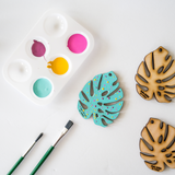 painted baby bare leaf with teal paint and pink and yellow polka dots placed beside a color palatte and paint brushes