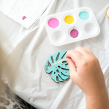 leaf cut out being painted with teal color and decorated with pink and yellow polka dots with a color palate near it