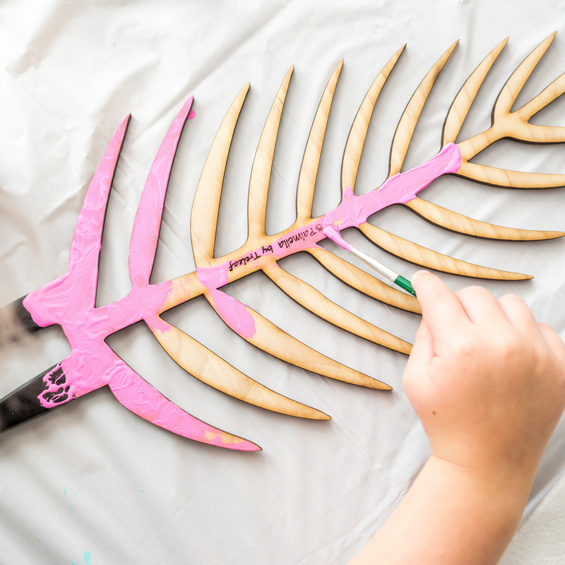 hand painting a wooden laser cut plant support with pink paint with engraving palmella by treleaf